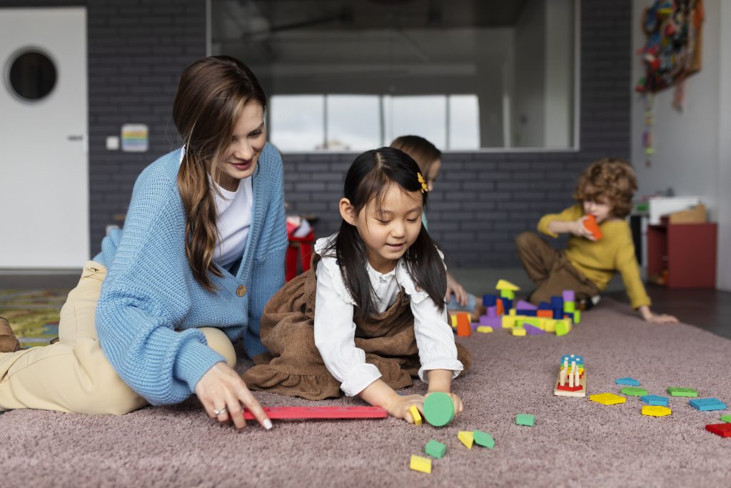 full-shot-smiley-teacher-helping-girl-learn (1) Montessori การเรียนรู้ต่างวัยที่เติบโตไปด้วยกัน