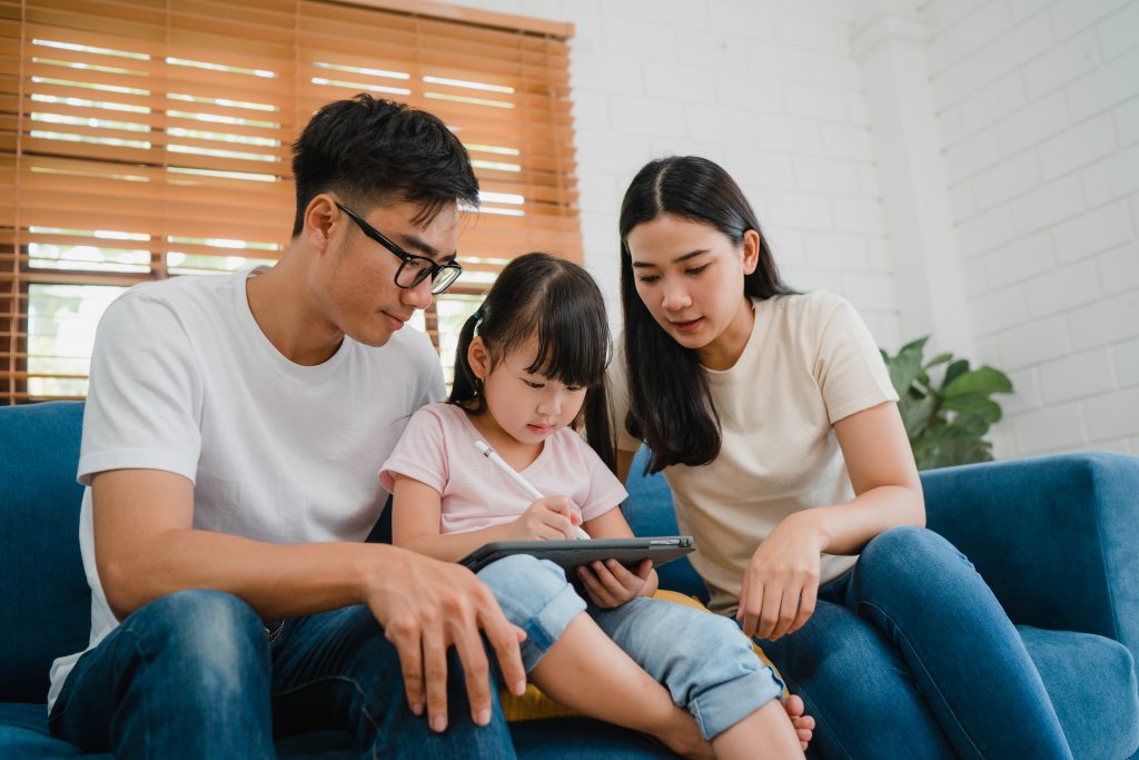 Happy Asian family dad, mom and daughter using computer tablet t พ่อแม่เลี้ยงลูก